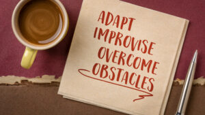 Coffee cup and pad of paper that says adapt, improvise, overcome obstacles