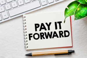 The words "Pay it Forward" printed on a notebook in front of a computer keyboard.