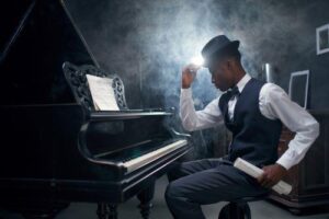 Vintage type photo of black man wearing bow tie, vest and hat and sitting at a piano