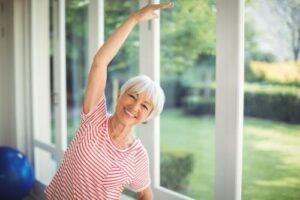 Smiling woman standing in front of window doing a side stretch
