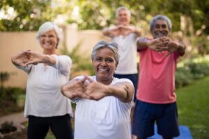 Group of 4 older adults standing outside and performing stretching exercise