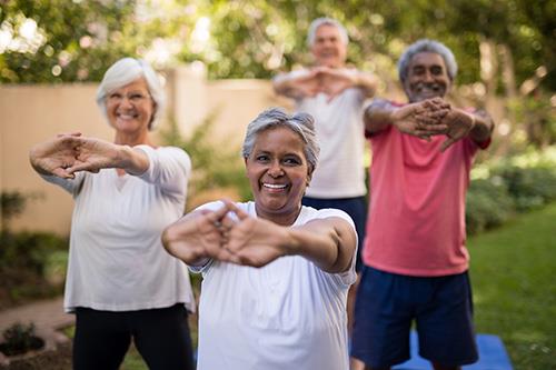 Group of 4 older adults standing outside and performing stretching exercise